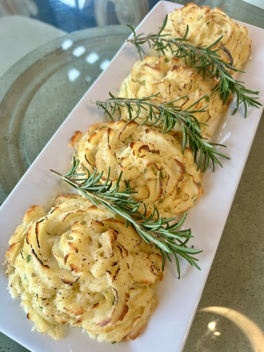 Duchess Potatoes served on a platter with sprigs of rosemary.